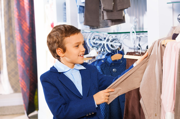 Cute smiling boy stands near clothes and choosing - Fotografie, Obrázek