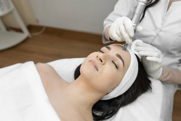 A professional cosmetologist uses innovative fractional mesotherapy to improve the condition of the skin in a beauty salon. The young woman is relaxed and rests during cosmetic procedures. High - Foto, Imagem