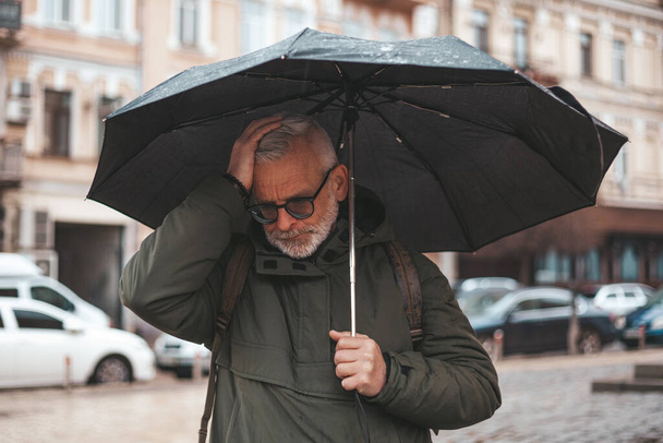 Headache in a mature man outdoors. Senior man under umbrella during doja with migraine. - Fotó, kép