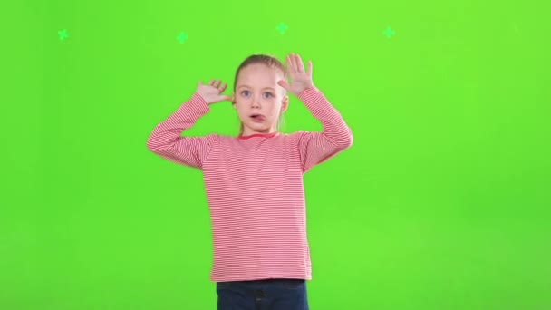 Αστεία αξιολάτρευτο κορίτσι κάνει αστεία πρόσωπα, ενώ κοιτάζοντας κάμερα στο στούντιο. Ένα όμορφο θηλυκό παιδί να πειράζει, να βγάζει γλώσσα, να σηκώνει χέρια, απομονωμένο στο πράσινο, σε κίνηση. Έννοια της έκφρασης, πειράγματα. - Πλάνα, βίντεο
