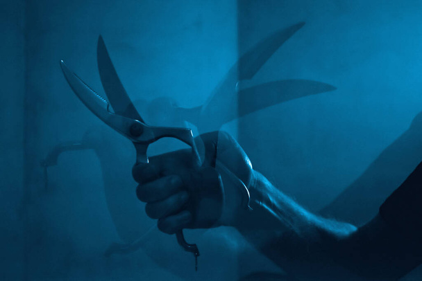hombre mano sosteniendo tijera en habitación azul oscuro - Foto, imagen