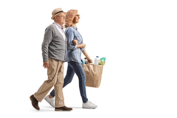 Full length profile shot of a woman helping an elderly man and carrying grocery bags isolated on white background - Valokuva, kuva