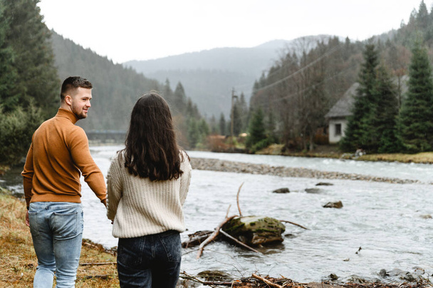 beautiful couple hugging and admiring each other while being in nature while traveling. lovers spend time together near the river overlooking the dense forest - Foto, Imagen