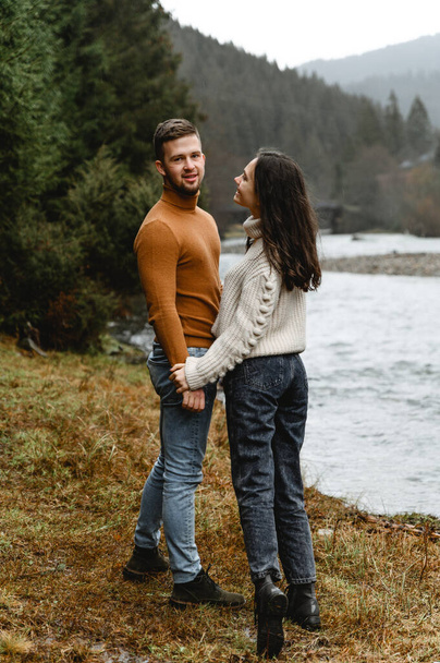 couple outdoors in the autumn season. lovers walk in a mountainous area near the river and forest. pastime of lovers during travel - Foto, Imagem