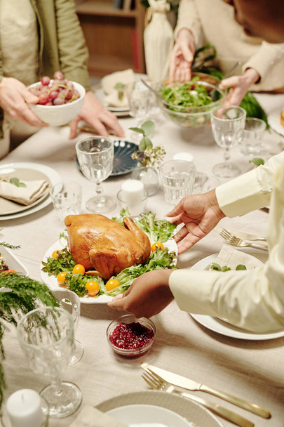 Handen van jonge zwarte vrouw zet bord met geroosterde kalkoen en verse groene sla en gele kerstomaten op tafel - Foto, afbeelding