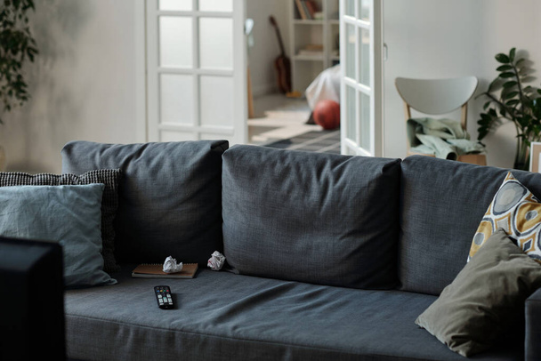 Harmaa mukava sohva useita pehmeitä tyynyjä seisoo keskellä olohuone vastaan avoin ovi ja osa kodikas makuuhuone - Valokuva, kuva