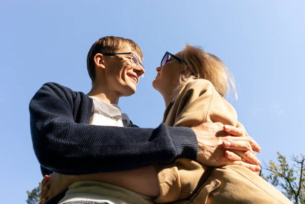 Hugging Happy Smiling Couple Looking At Eyes Of One Another, Blue Sky On Background. Relationship, Togetherness. Enjoying Time Together. Feelings. Vertical Plane Summer Time. High quality photo - 写真・画像