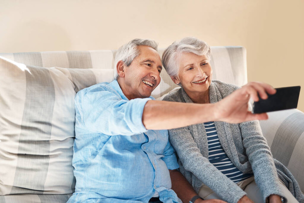 Vanhempi pari, selfie ja hymy sohvalla onnea sosiaalisessa mediassa, blogissa tai postitse internetissä. Vanhukset mies, nainen ja valokuvaus profiilikuva app, web tai onnellinen yhdessä sohvalla kotona. - Valokuva, kuva