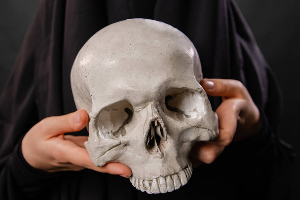close-up of a human skull in the hands of a woman dressed in a black robe - Фото, зображення
