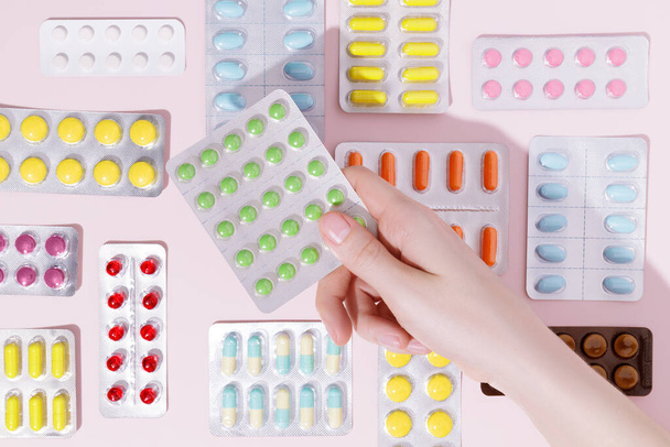 Hand holding pills in blister packs on a pink background. Health care concept. Top view. - Foto, imagen