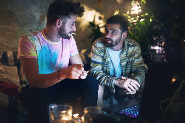 Let me light this up...watch how I smoke it. a handsome young man lighting up a joint of cannabis while sitting with is friend at home - Foto, imagen