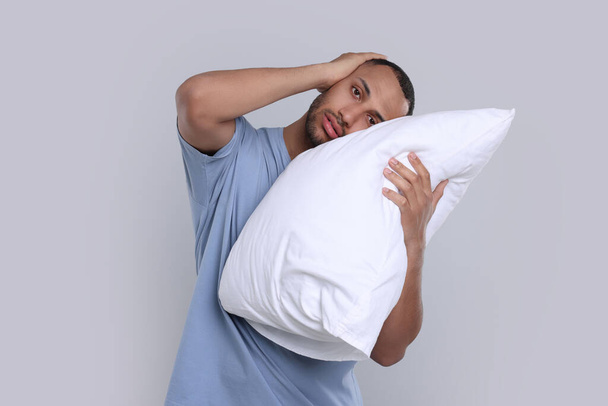 Sleepy man with pillow on light grey background. Insomnia problem - Zdjęcie, obraz