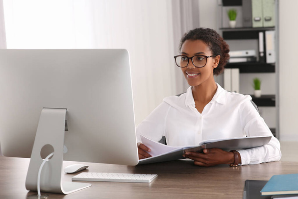 African American intern with folder working at table in office - Фото, зображення