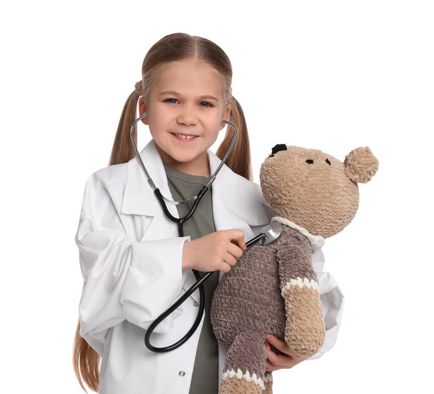 Little girl playing doctor with toy bear on white background - Foto, Imagen