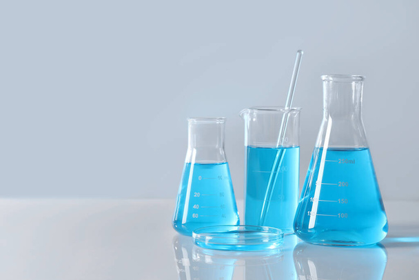 Different laboratory glassware with light blue liquid on table, space for text - 写真・画像