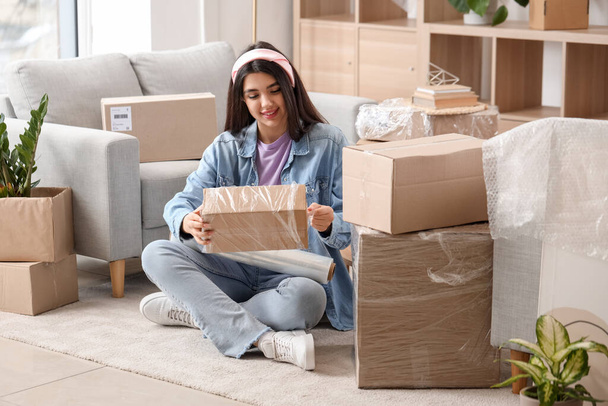 Молодая женщина упаковывает картонную коробку с пленкой для растяжки дома в день переезда - Фото, изображение