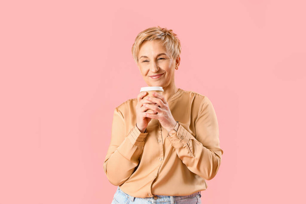 Dreaming mature woman with cup of coffee on pink background - Photo, image
