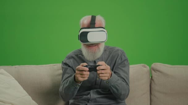 Écran vert. Un vieil homme avec des lunettes VR joue à des jeux informatiques avec un joystick, assis sur un canapé. Un homme âgé joue à PlayStation et gagne. La nostalgie technologique et le fossé générationnel. - Séquence, vidéo