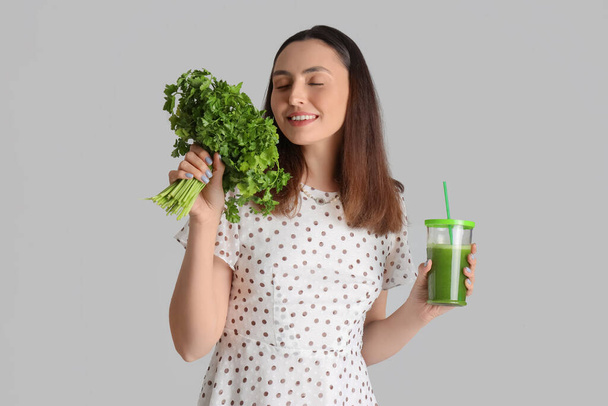 Young woman with glass of vegetable juice and parsley on grey background - Foto, Imagem