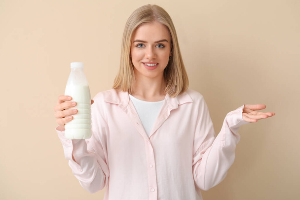 Beautiful young woman with bottle of milk on beige background - 写真・画像