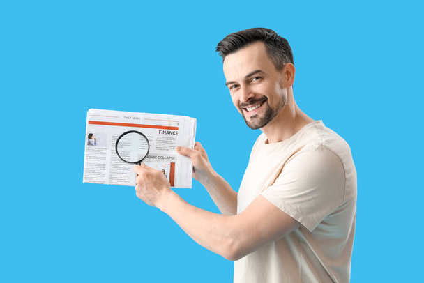 Handsome man with magnifier and newspaper on blue background - Foto, imagen