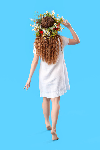 Beautiful young woman in flower wreath on blue background, back view. Summer solstice - Valokuva, kuva
