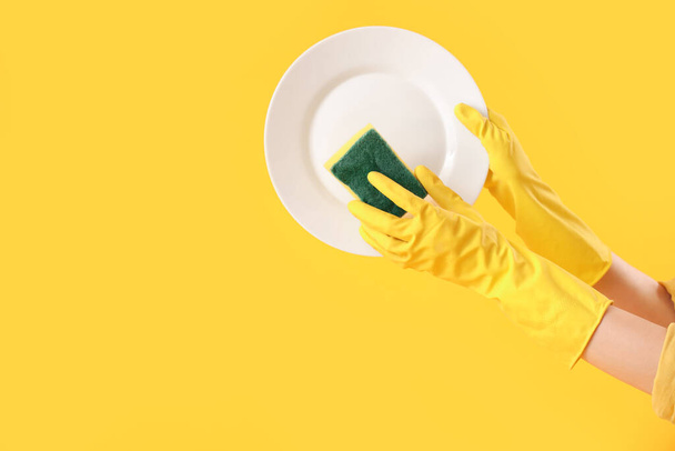 Női kezek tányérral és szivaccsal sárga alapon - Fotó, kép
