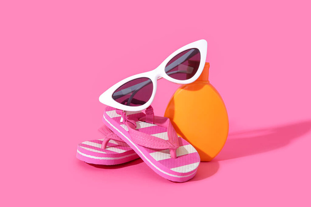 Bouteille de crème solaire avec lunettes de soleil et tongs sur fond rose - Photo, image