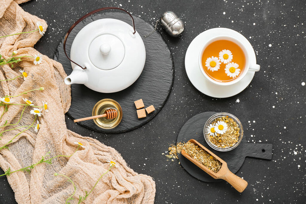 Cup of hot chamomile tea and teapot on dark background - Fotó, kép