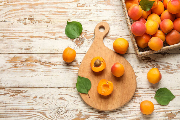 Board and wicker box with fresh apricots on white wooden background - Zdjęcie, obraz