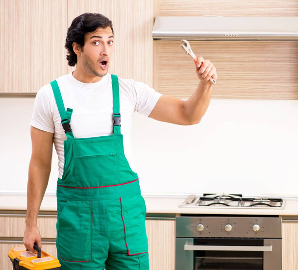 Der junge Bauunternehmer repariert den Ofen in der Küche - Foto, Bild
