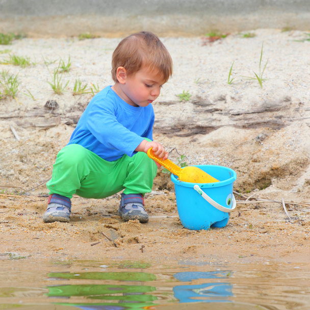 Маленький хлопчик грає з відром і лопатою
 - Фото, зображення