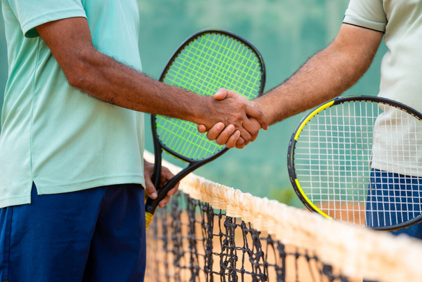コートでテニスの試合をする前に握手をすることで、インドの高齢者の友人たちの挨拶のショットを閉じます-エンターテイメント、競争、退職生活の概念. - 写真・画像