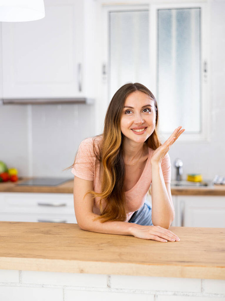 Young girl in casual clothes posing with elbows on table in light kitchen - Foto, immagini