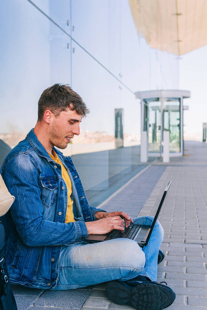 Foto vertical de um homem sentado na rua usando um laptop - Foto, Imagem
