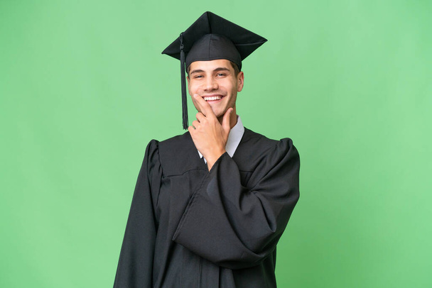 Mladý vysokoškolský absolvent kavkazský muž přes izolované pozadí s úsměvem - Fotografie, Obrázek