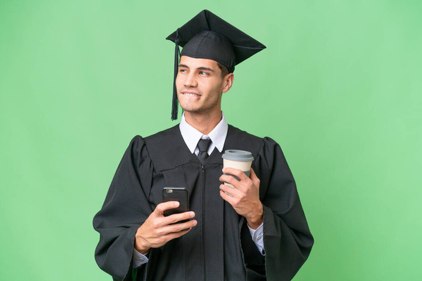 Young university graduate caucasian man over isolated background holding coffee to take away and a mobile while thinking something - 写真・画像