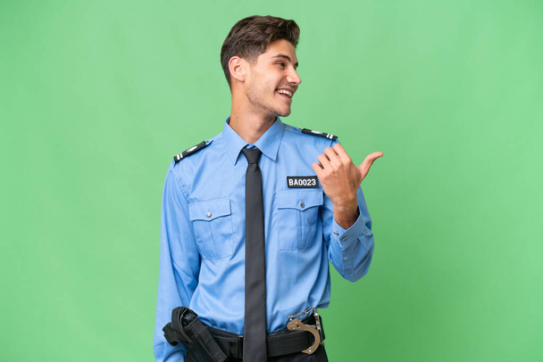 Junger Polizist mit isoliertem Hintergrund zeigt zur Seite, um ein Produkt zu präsentieren - Foto, Bild