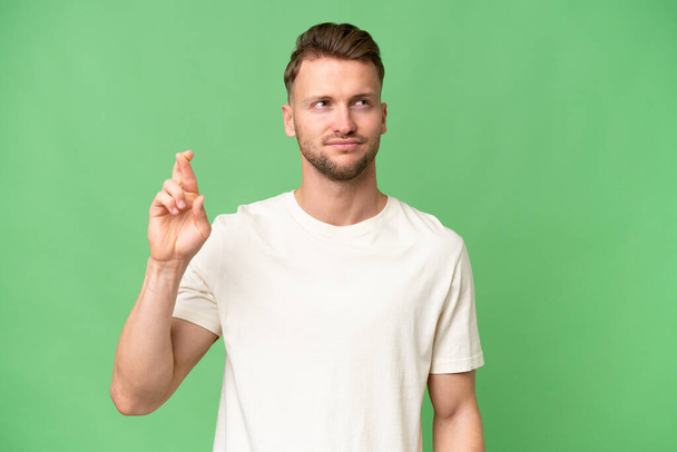 Young blonde caucasian man over isolated background with fingers crossing and wishing the best - Photo, Image