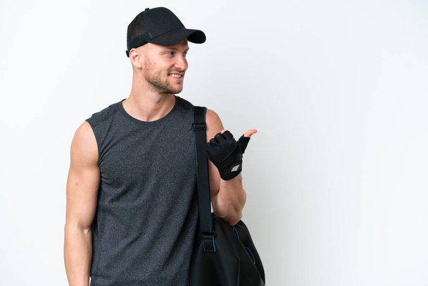 Young blonde sport caucasian man with sport bag over isolated white background pointing to the side to present a product - Photo, Image