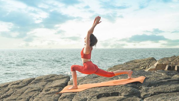 giovane donna in un abbigliamento sportivo rosso sta eseguendo un tratto di yoga sulla riva dell'oceano. Foto di alta qualità - Foto, immagini