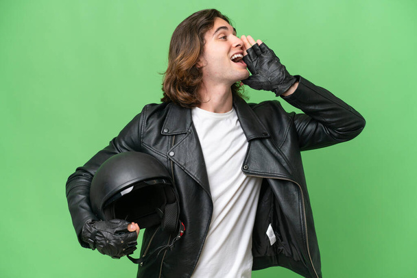 Νεαρός όμορφος άνδρας με κράνος μοτοσικλέτας απομονωμένος στο πράσινο chroma φόντο φωνάζοντας με το στόμα ορθάνοιχτο στο πλάι - Φωτογραφία, εικόνα