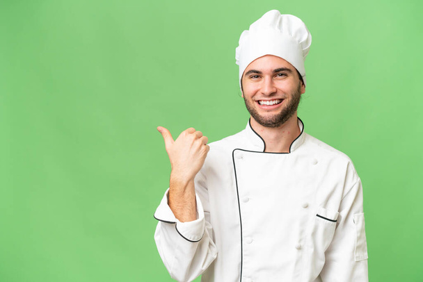 Nuori komea kokki mies yli eristetty tausta osoittaa sivulle esittää tuotteen - Valokuva, kuva