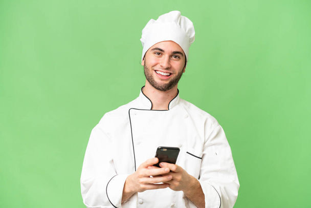 Young handsome chef man over isolated background sending a message with the mobile - Fotó, kép