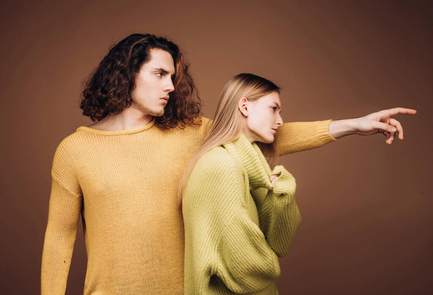 Portret of stylish confident male and female models with nature hairstyle wearing a yellow and green sweater and standing close together looking alluringly at camera - 写真・画像