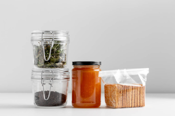 food, healthy eating and diet concept - jars with dried herbs, tea, jam and cookies on white background - 写真・画像