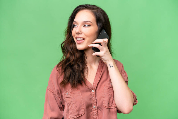 Молодая белая женщина на изолированном фоне ведет разговор с кем-то по мобильному телефону - Фото, изображение