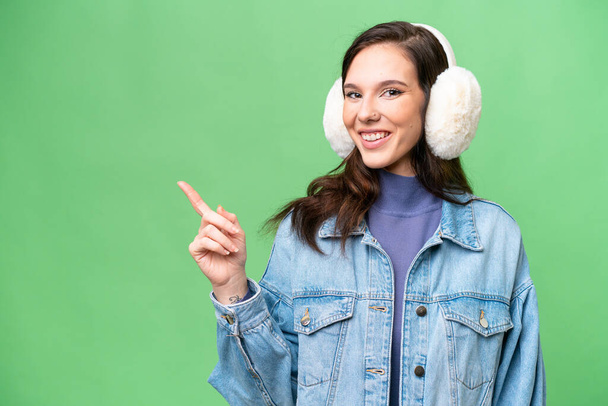 Young caucasian woman wearing winter muffs over isolated background pointing finger to the side - Photo, Image