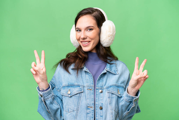 Young caucasian woman wearing winter muffs over isolated background showing victory sign with both hands - Photo, Image