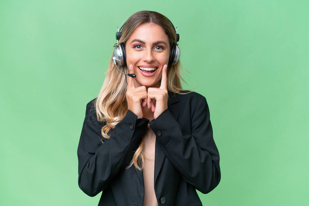 Telemarketer pretty Uruguayan woman working with a headset over isolated background smiling with a happy and pleasant expression - Photo, image